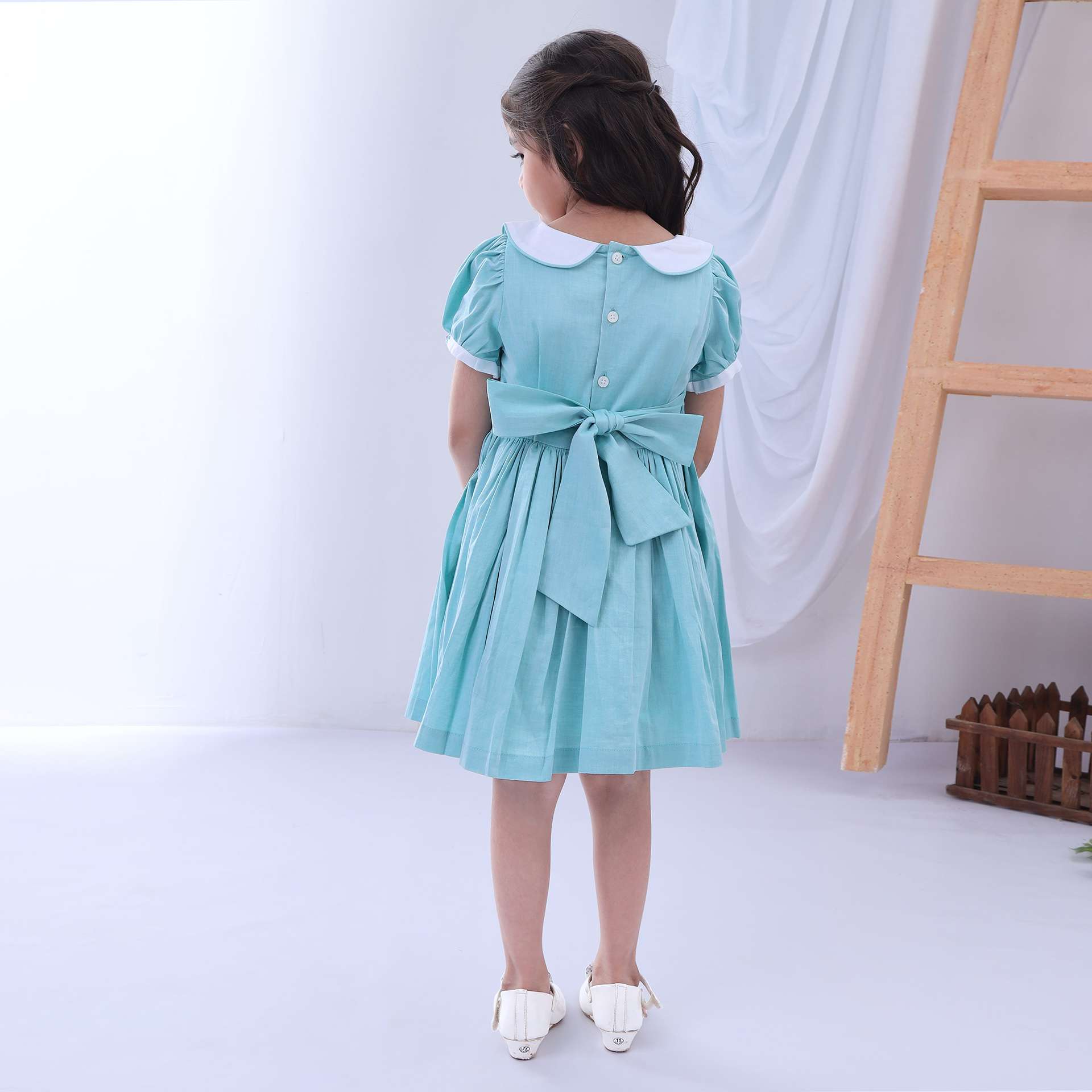 Rear image of a girl in turquoise hand smocked cotton dress