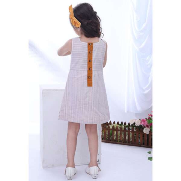 Rear image of a little girl in cream sleeveless dress with hand embroidered pocket and lace trims on hems