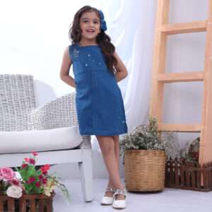 Girl leans against a cane chair wearing a deep blue A-line dress with birdcage hand embroidery