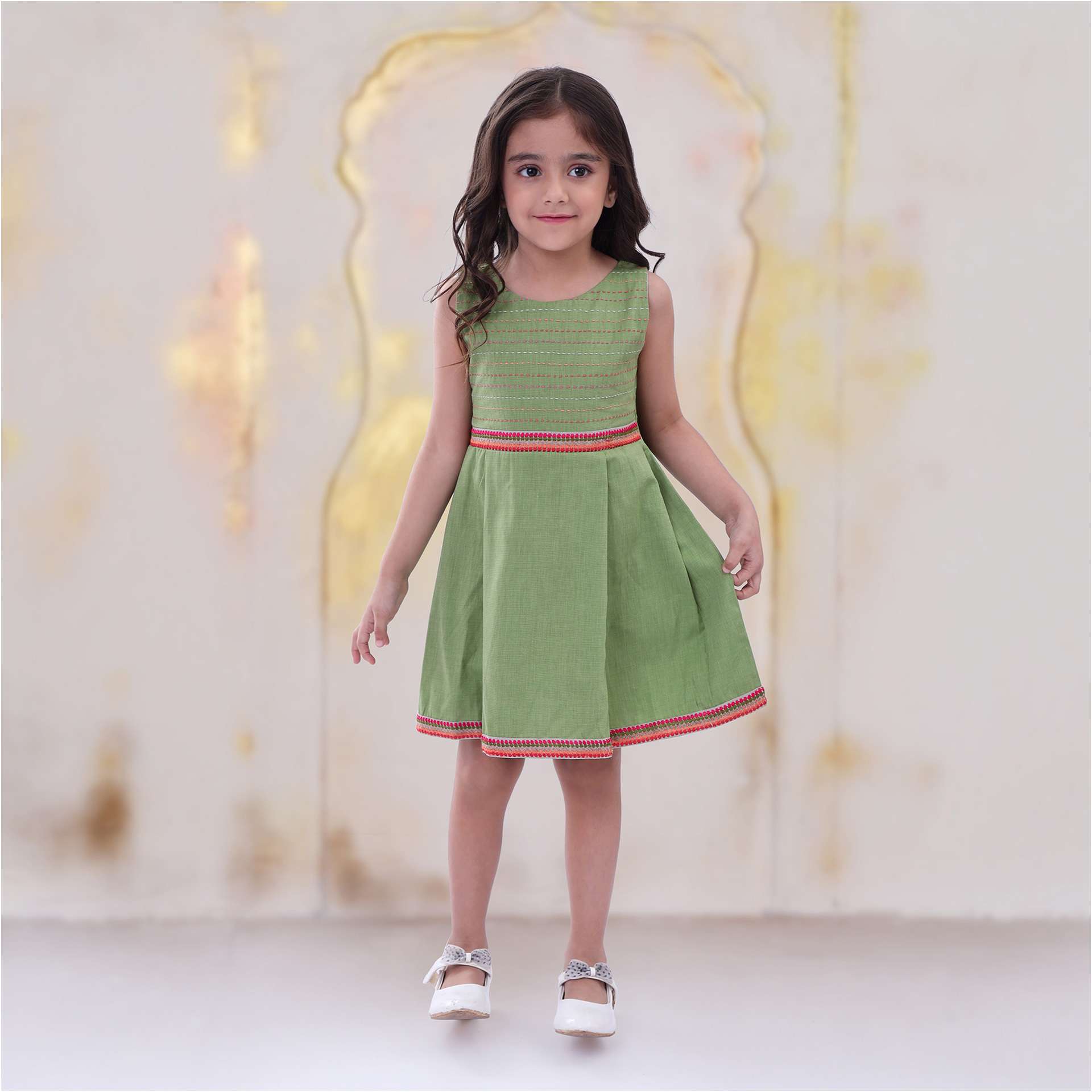 A little girl in green cotton dress with a Kantha hand embroidered bodice and colourful waistline and hem