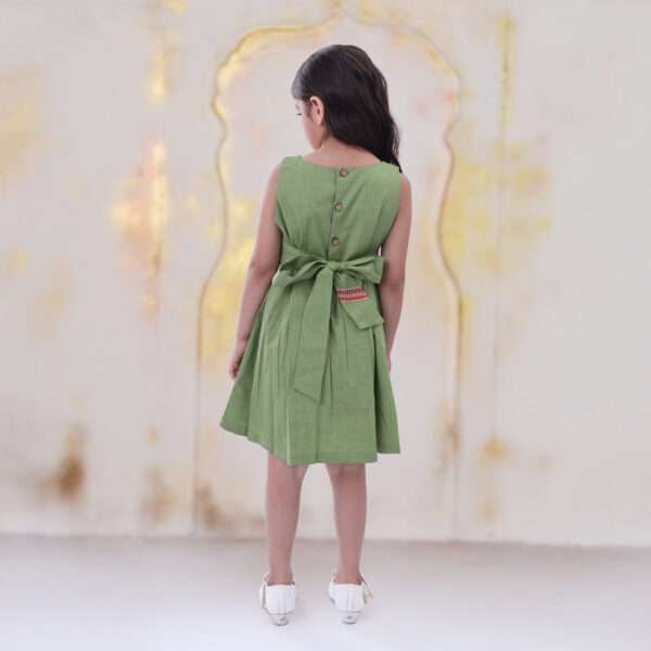 Rear image of a little girl in green sleeveless dress with hand embroidered border detail and back belt