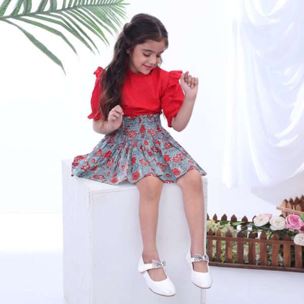 A little girl in teal and coral chinoiserie print skirt with blouse in red swissdot with ruffled collar