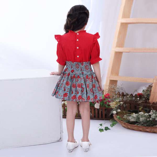 Rear image of a little girl in teal and coral chinoiserie print skirt with blouse in red swissdot with ruffled collar