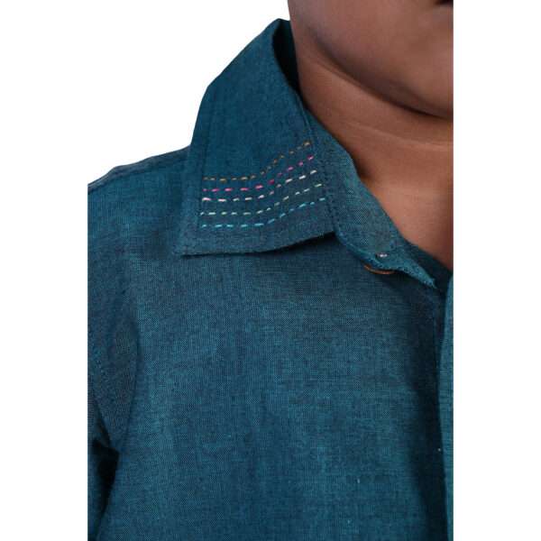 Close up of a boy wearing a teal chambray shirt- the collar has hand embroidery detailing