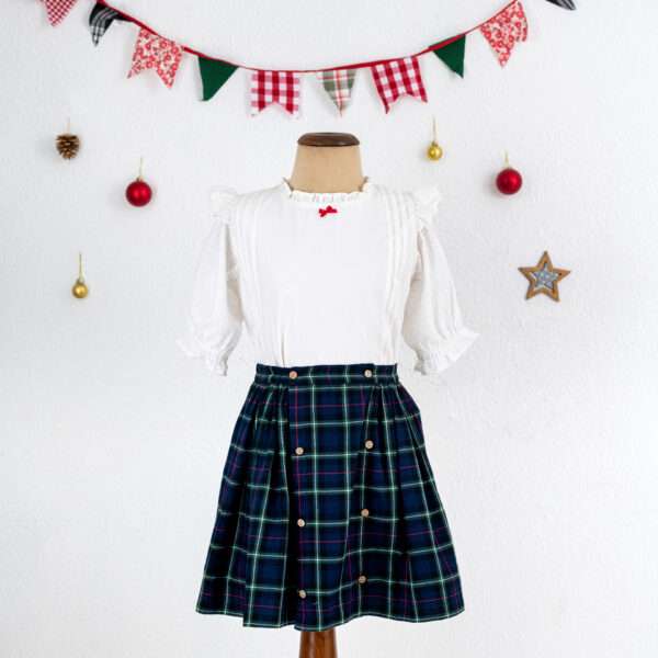 Mannequin shot of navy tartan wrap skirt paired with a frilly white cotton blouse with a little red satin bow