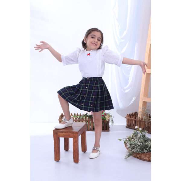 A little girl posing in navy tartan wrap skirt paired with a frilly white cotton blouse with a little red satin bow