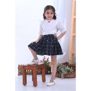 A little girl in navy tartan wrap skirt paired with a frilly white cotton blouse with a little red satin bow