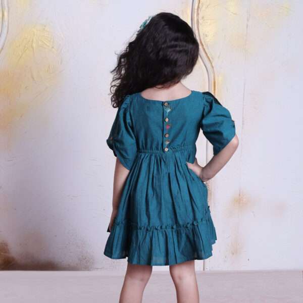 Rear image of a little girl in a peacock blue dress with bead work and hand embroidery on front and back bodice with wooden buttons in the back and gathered sleeve panels