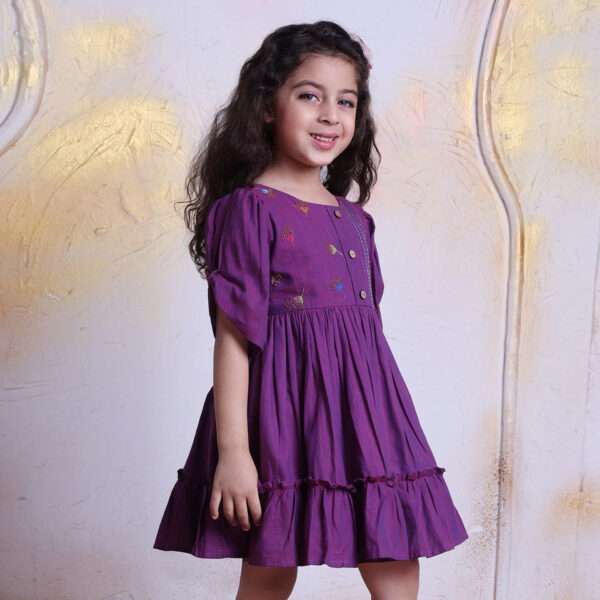 Girl wearing berry pink cotton dress with a hand embroidered bodice decorated with wooden buttons