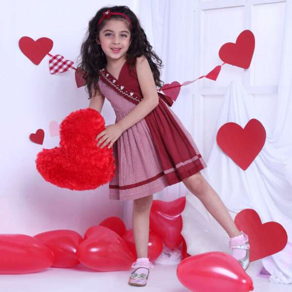 A girl in red checked dress with a hand-smocked band of hearts in a crossover style, with a V-neck and cord piping trims