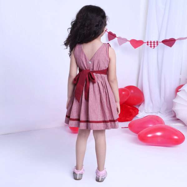 Rear image of a girl in red checked dress with a hand-smocked band of hearts in a crossover style and cord piping trims
