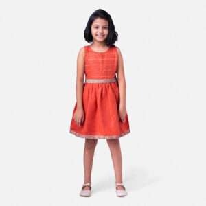 A little girl in a burnt orange hand embroidered linen dress with matching shorts