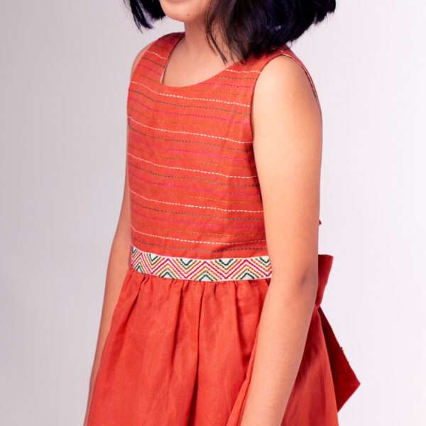 A girl in chic burnt-orange linen dress with colourful embroidered waistline with a Kantha-work hand-embroidered bodice