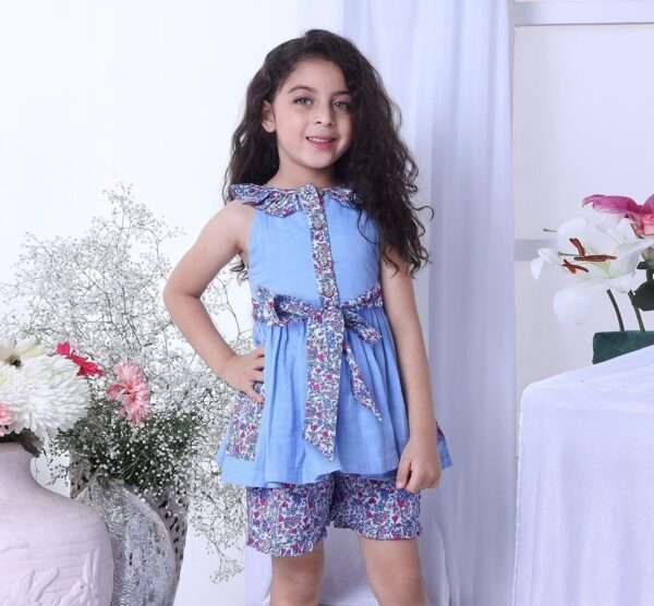 A girl in blue double gauze cotton tunic with floral ruffled neckline and tie-up belt paired with matching floral shorts