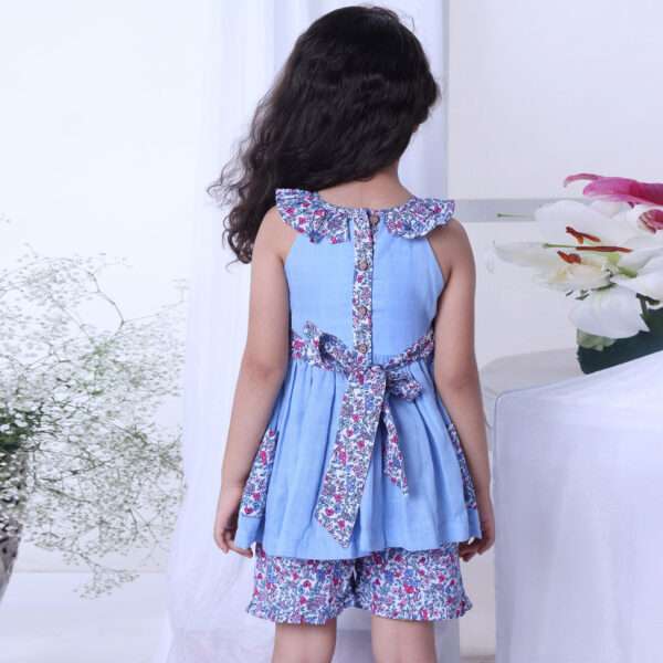 A girl in blue double gauze cotton tunic with floral ruffled neckline and tie-up belt paired with matching floral shorts