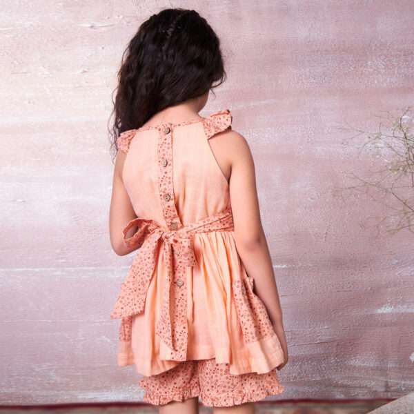 Rear image of a girl in peach gauze tunic with hand embroidery, ruffles and ties in a floral trim, with matching shorts