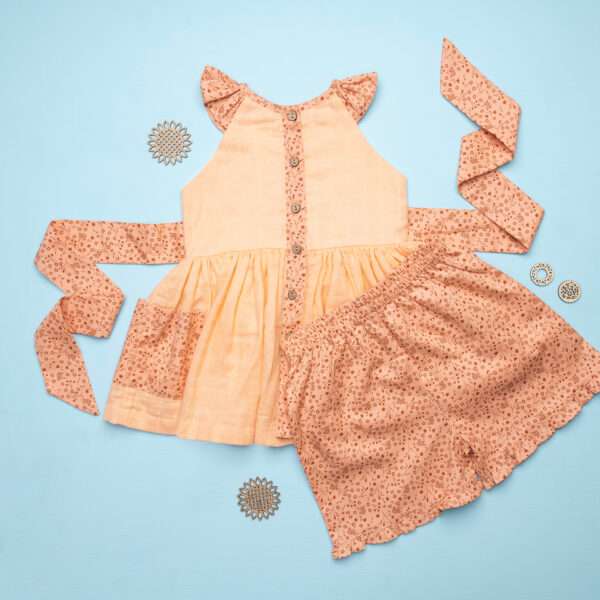 Flatlay of peach gauze tunic with ruffles, hand embroiSoleilclo_259_Hdery and ties in a floral trim, with matching floral shorts