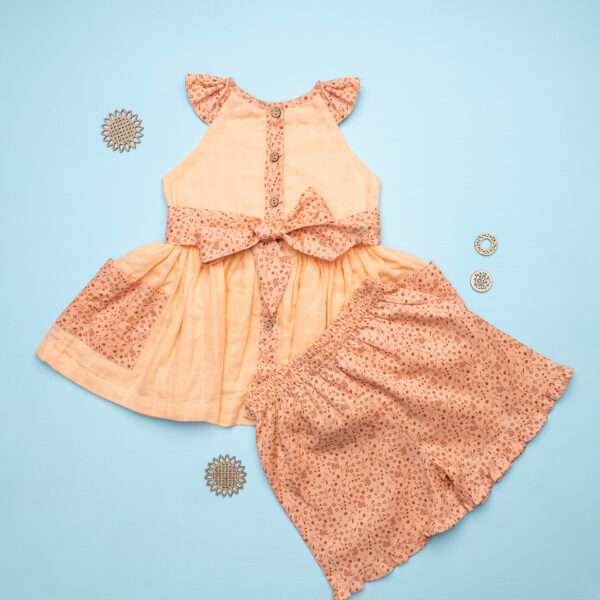 Flatlay of peach gauze tunic with ruffles, hand embroidery and ties in a floral trim, with matching floral shorts