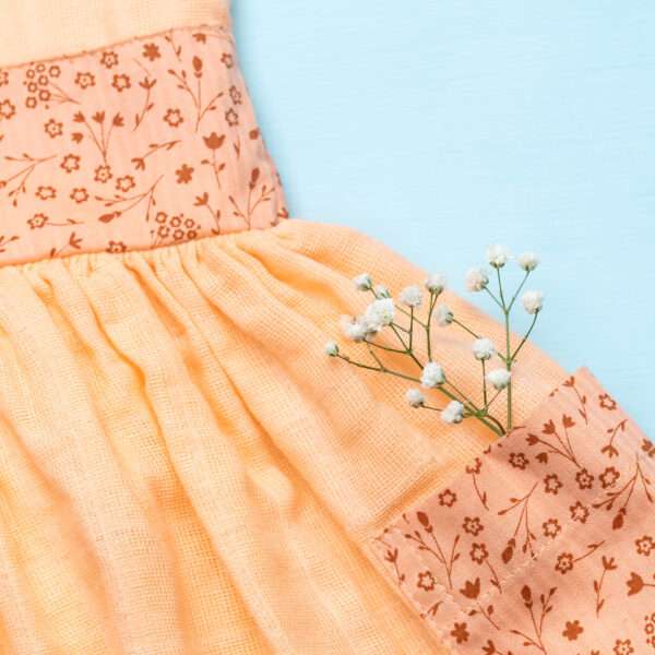 Close-up of pocket in peach gauze tunic with ruffles, hand embroidery and ties in a floral trim