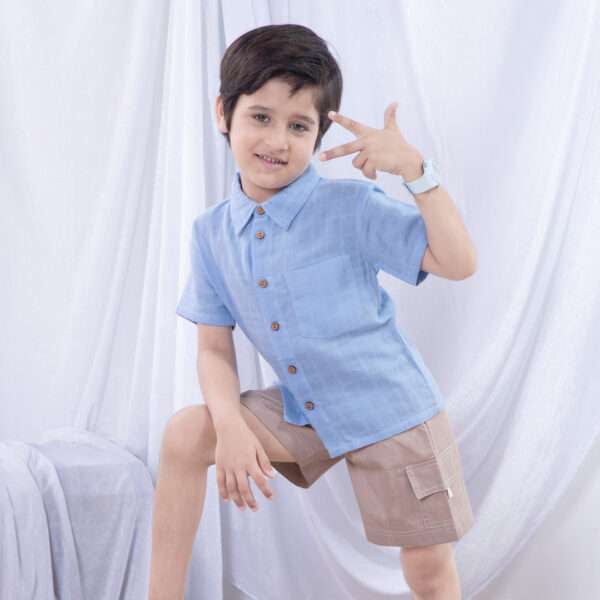 A little boy in light blue button down gauze shirt with wood buttons paired with tan cargo shorts