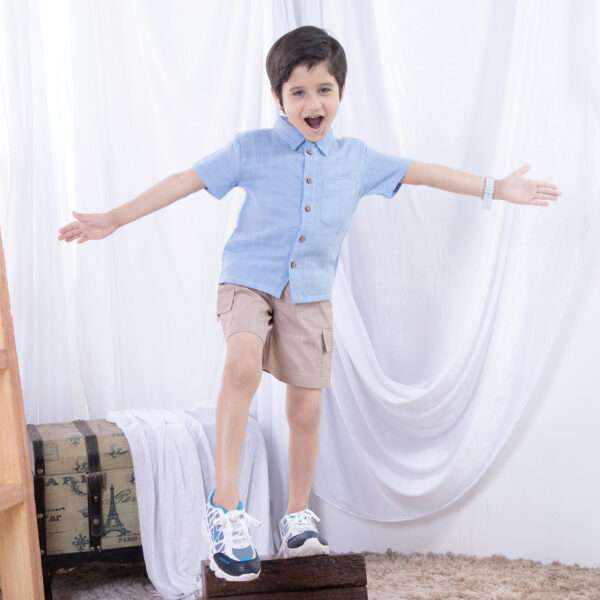 A cheeky little boy in light blue button down gauze shirt with wood buttons paired with tan cargo shorts
