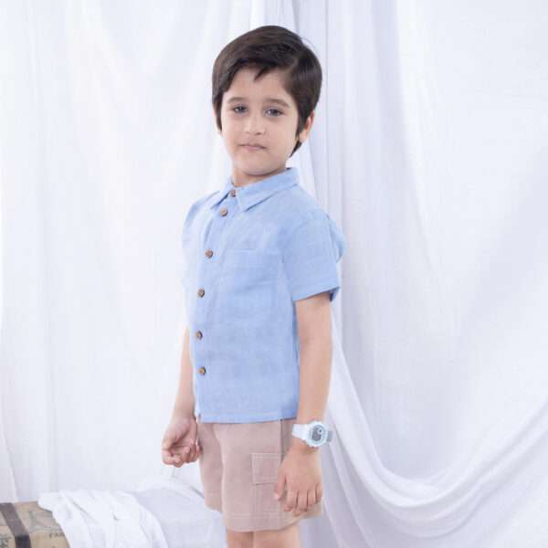 A little boy in light blue button down gauze shirt with wood buttons paired with tan cargo shorts