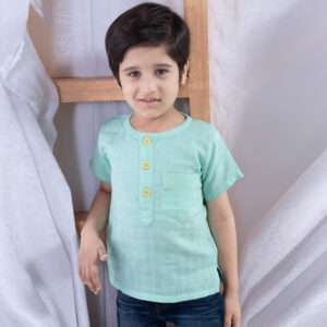 Boy leans against a ladder wearing an aqua gauze shirt with round neckline and yellow buttons