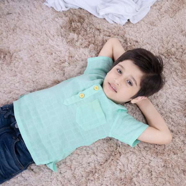 A boy in aqua gauze boy's shirt with hand embroidered front pocket and yellow buttons
