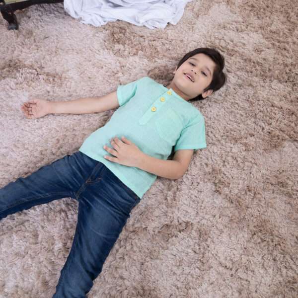 A boy laying down wearing aqua gauze boy's shirt with hand embroidered front pocket and yellow buttons