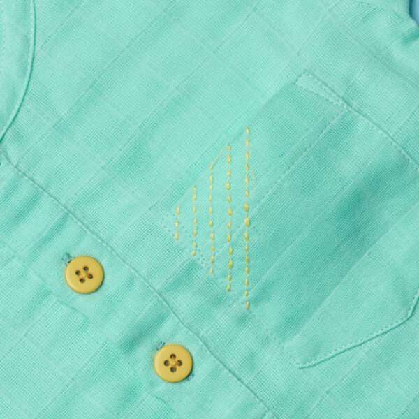An aqua green shirt pocket is seen with kantha work diagonal stitching on the pocket and a couple of matched yellow buttons