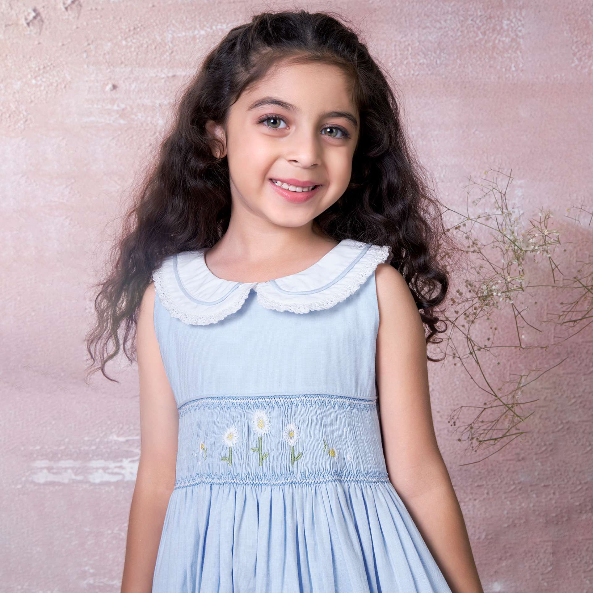 A little girl in blue hand-smocked dress with a lace insert on the skirt and a detailed collar with lace and cord piping