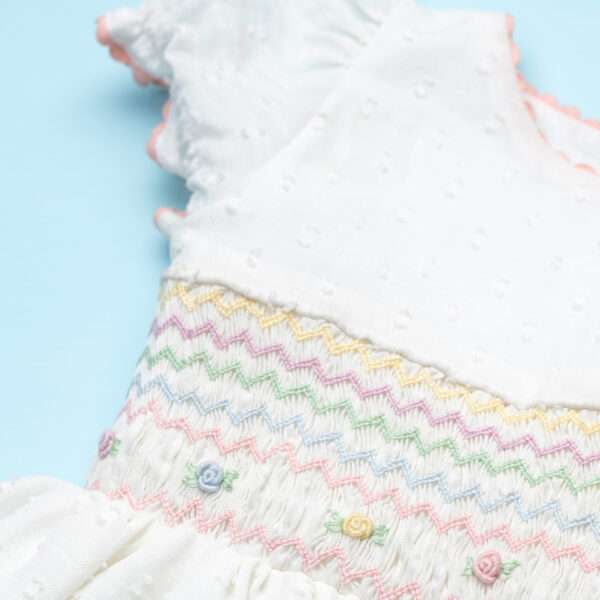 Close-up of a flatlay of a hand-smocked georgette swiss-dot dress with ric-rac trims and pastel floral embroidery