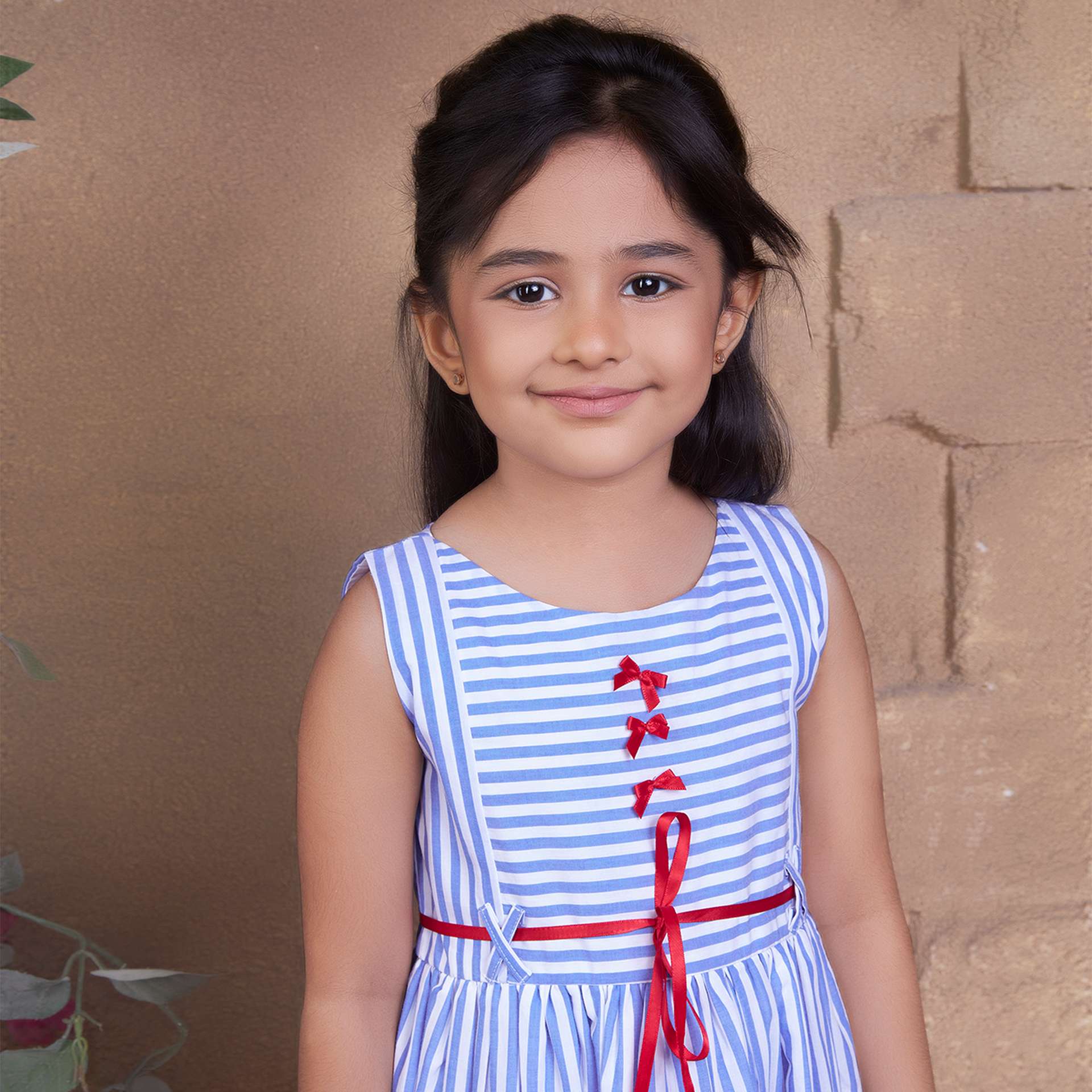 Girl smiling wearing a blue stripe sleeveless outfit with red bows