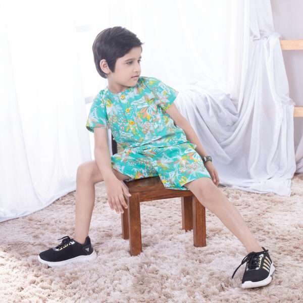 Boy leans back wearing an aqua half sleeve casual shirt in a jungle print with matched bermudas