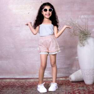 A little girl in cotton peach shorts, designed with a delicate touch of lace trims and hand embroidery on the pocket