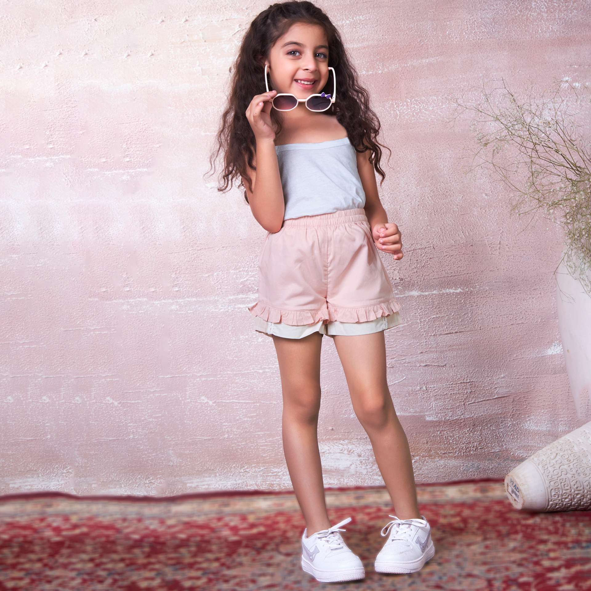 A little girl in cotton peach shorts, designed with a delicate touch of lace trims and hand embroidery on the pocket