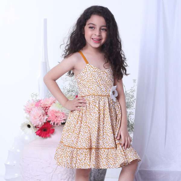 A little girl wearing strappy shoulder dress with floral print in mustard and big flower appliqued on the waist