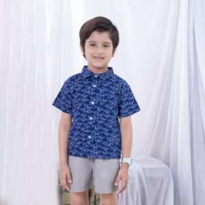 A little boy in navy blue boy's shirt in shark print with buttons down the front