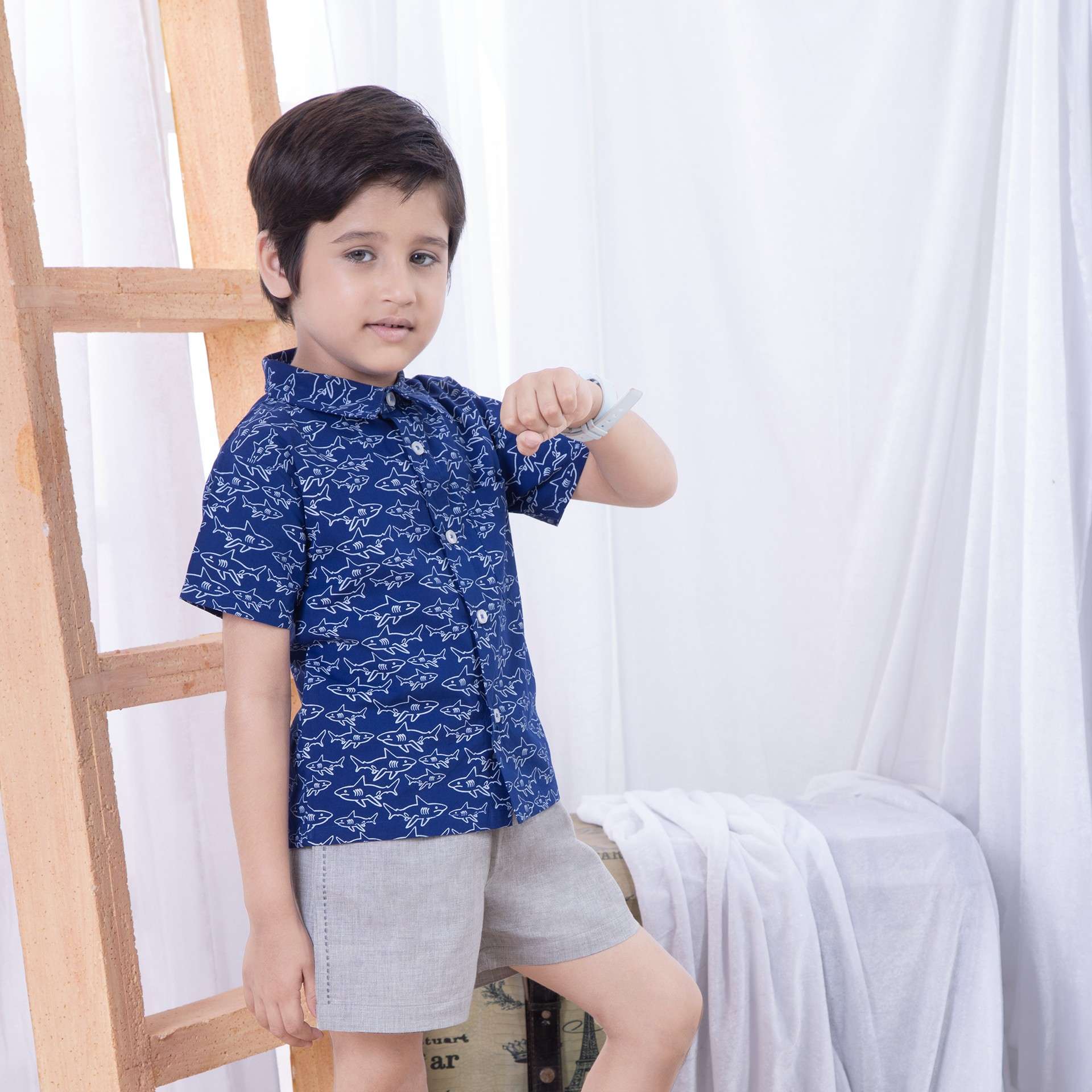 A little boy in blue shark print shirt paired with grey shorts