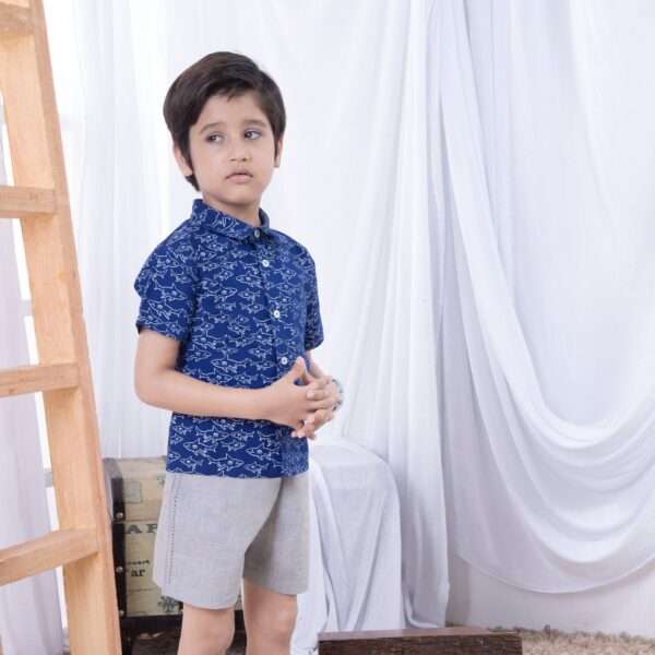 A little boy in blue shark print shirt paired with grey shorts