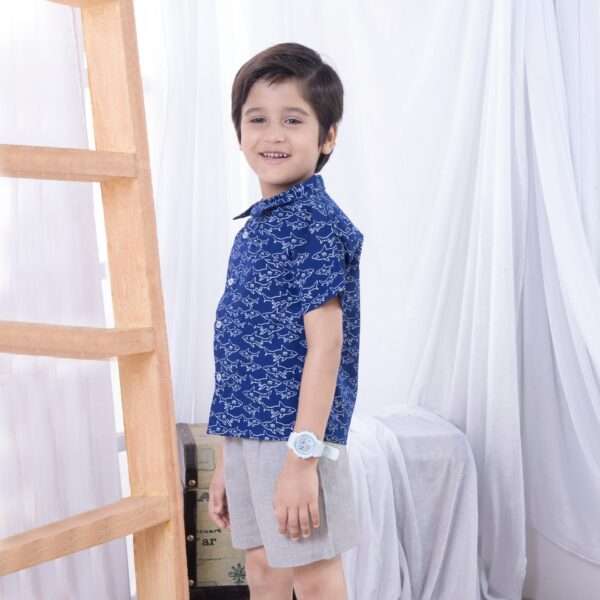 A little boy in navy blue shark print shirt with buttons down the front paired with grey shorts