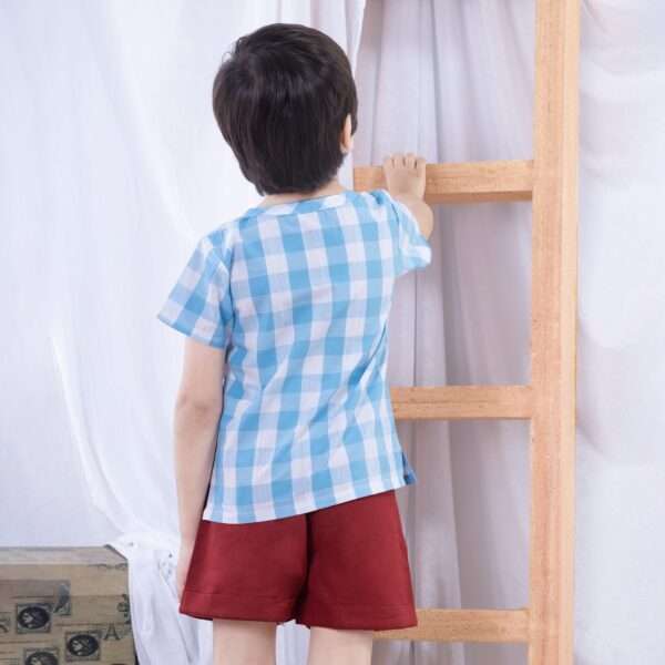 Boy tries to climb up a ladder wearing abig blue check shirt and red shorts