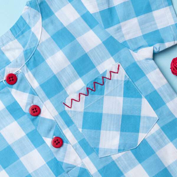 Close up of light blue checked shirt with red chevron hand embroidered front pocket and bright red buttons