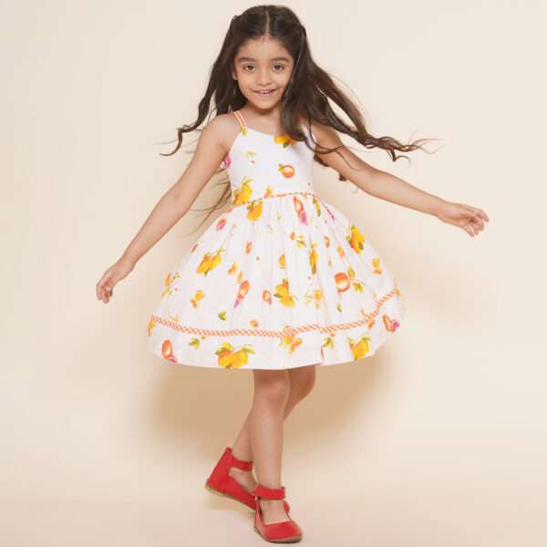 A little girl in pink vibrant fruit print dress with lemons, tangerines and daisies and orange gingham trims