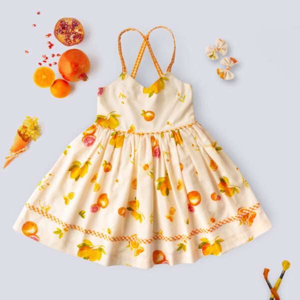 Flatlay of pink vibrant fruit print dress with lemons, tangerines and daisies and orange gingham trims