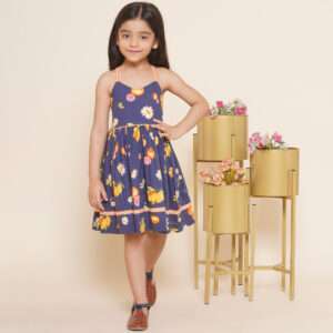 A young girl wearing a strappy shoulder floral and fruit printed navy dress with contrast trims