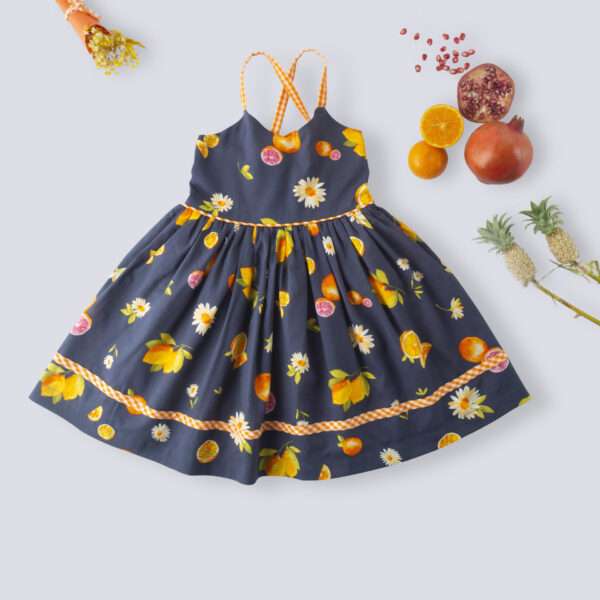 Flatlay of strappy vibrant fruit printed dress with orange gingham trims, shirred back and tie-up straps