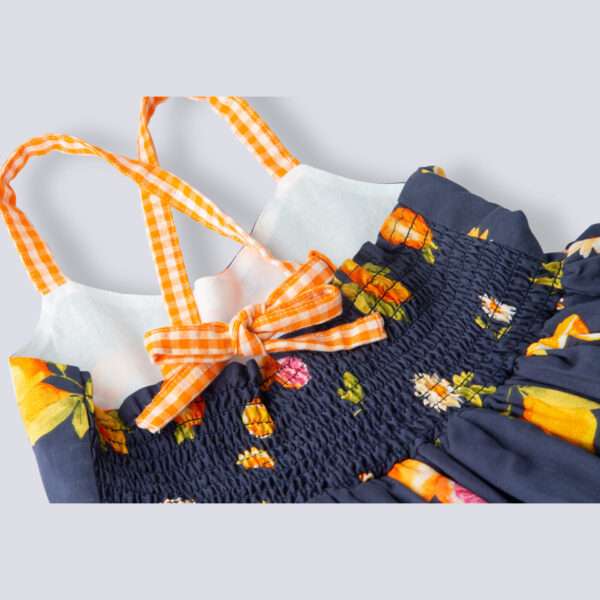 Close-up flatlay of strappy vibrant fruit printed dress with orange gingham trims, shirred back and tie-up straps