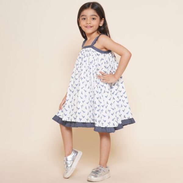 A little girl in strappy shoulder dress with blue bird print and tiny ruffles on the shoulder straps in navy dot fabric