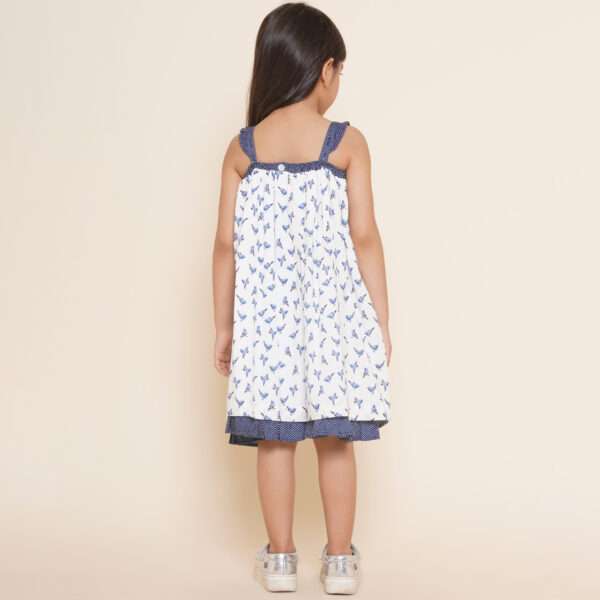 Rear side of girl in strappy shoulder dress with blue bird print and ruffles on the shoulder straps in navy dot fabric